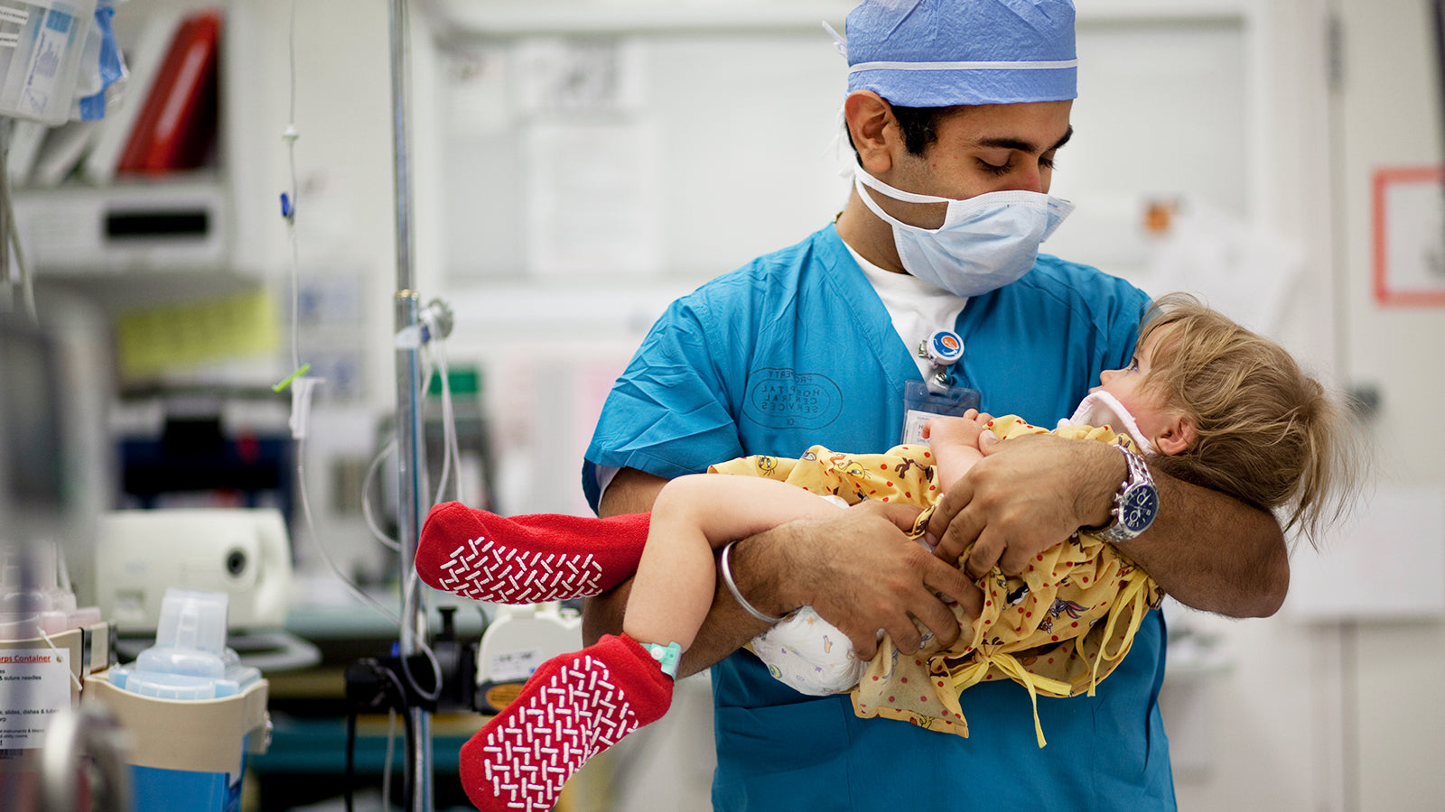 A male doctor holds a sick child in his arms.